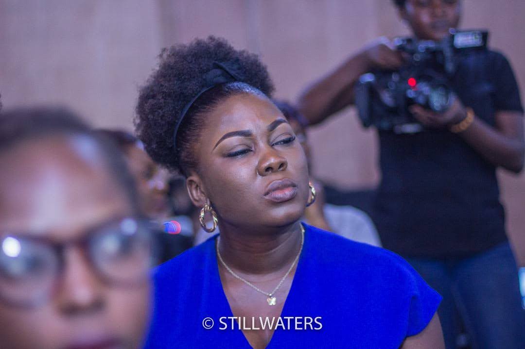 A woman experiences a moment of spiritual renewal with her eyes closed in worship during a Stillwaters Ministries service. A camera operator is visible in the background.
