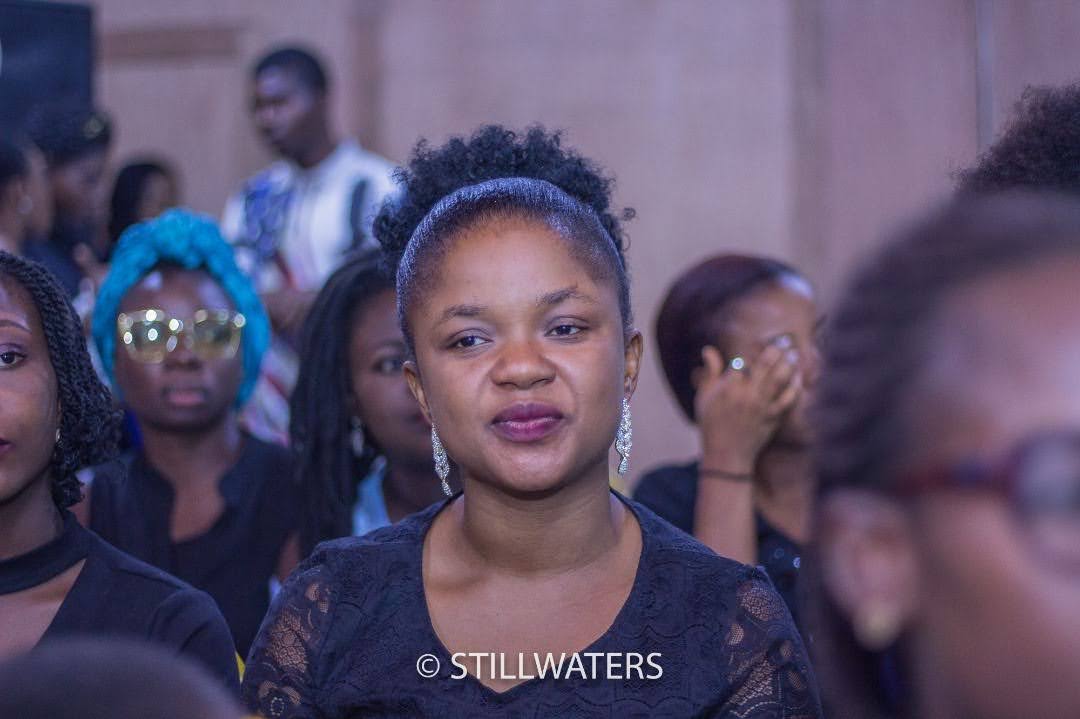 A woman with her hair in a high puff looks on attentively while seated in the congregation during a Stillwaters Ministries event.