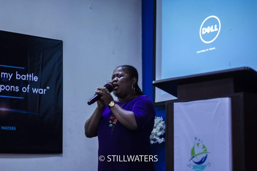 A woman leads worship, singing passionately into a microphone during a Stillwaters Ministries conference.